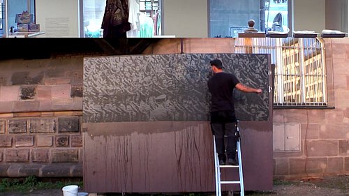 Eine große Cortenstahlplatte wird mit einer Schwarzweißfotografie, die die Hitlerjugend während eines Reichsparteitagsgeländes zeigt