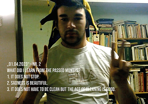 Videostill zeigt einen jungen Mann mit Narrenkappe, der mit beiden Händen das Victory-Zeichen in die Kamera hält