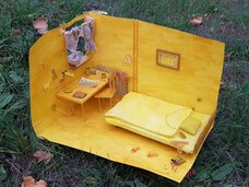 Blick von oben in das Modell eines Zimmers ganz in gelb gehalten. Zu sehen sind ein Bett, ein Schreibtisch vor dem Fenster und ein Bild an der Wand.