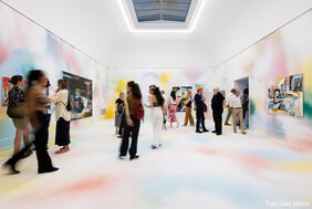 Blick in den Ausstellungsraum zwei, dessen Wände und Boden mit pastellfarbigen Farbwolken besprüht sind. An den Wänden noch die großformatigen Gemälde der Künstlerin.