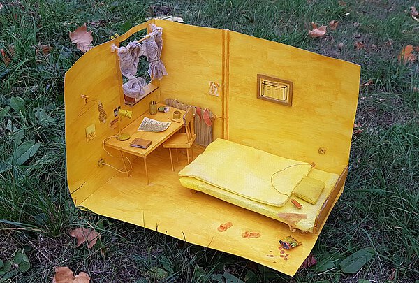 Blick von oben in das Modell eines Zimmers ganz in gelb gehalten. Zu sehen sind ein Bett, ein Schreibtisch vor dem Fenster und ein Bild an der Wand.