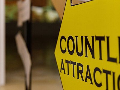 Ein großer gelber Pfeil bewirbt mit schwarzer Schrift die Ausstellung als Attraktion