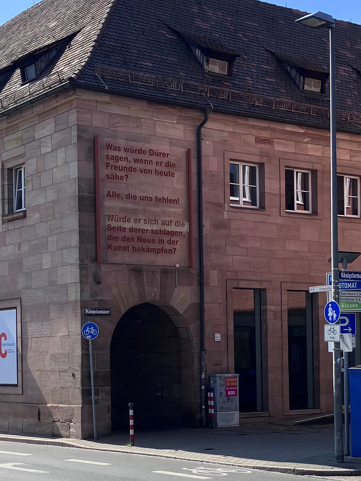 Steinernes historisches Gebäude mit Arkaden und großen Bannern. Auf einem Banner steht ein Text in roten Buchstaben.