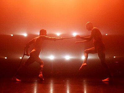 Zwei Fechter in Kampfhaltung mit Florett auf einer Bühne vor orangefarbener Beleuchtung