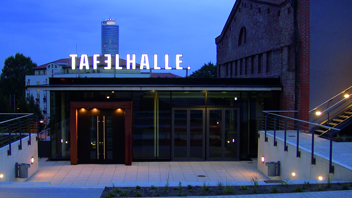 Eingang eines Gebäudes mit beleuchtetem Schriftzug 'TAFELHALLE' über Glastüren und Fenstern