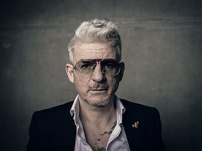 Mann mit grauen Haaren, Hemd, Krawatte und Weste vor neutralem Hintergrund