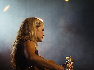 Nahaufnahme einer Frau mit langen Haaren, die eine Gitarre spielt, vor dunklem Hintergrund mit Lichtpunkten