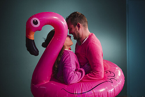 ein Mann und eine Frau in pinken Oberteilen in der Mitte eines aufblasbaren Flamingo