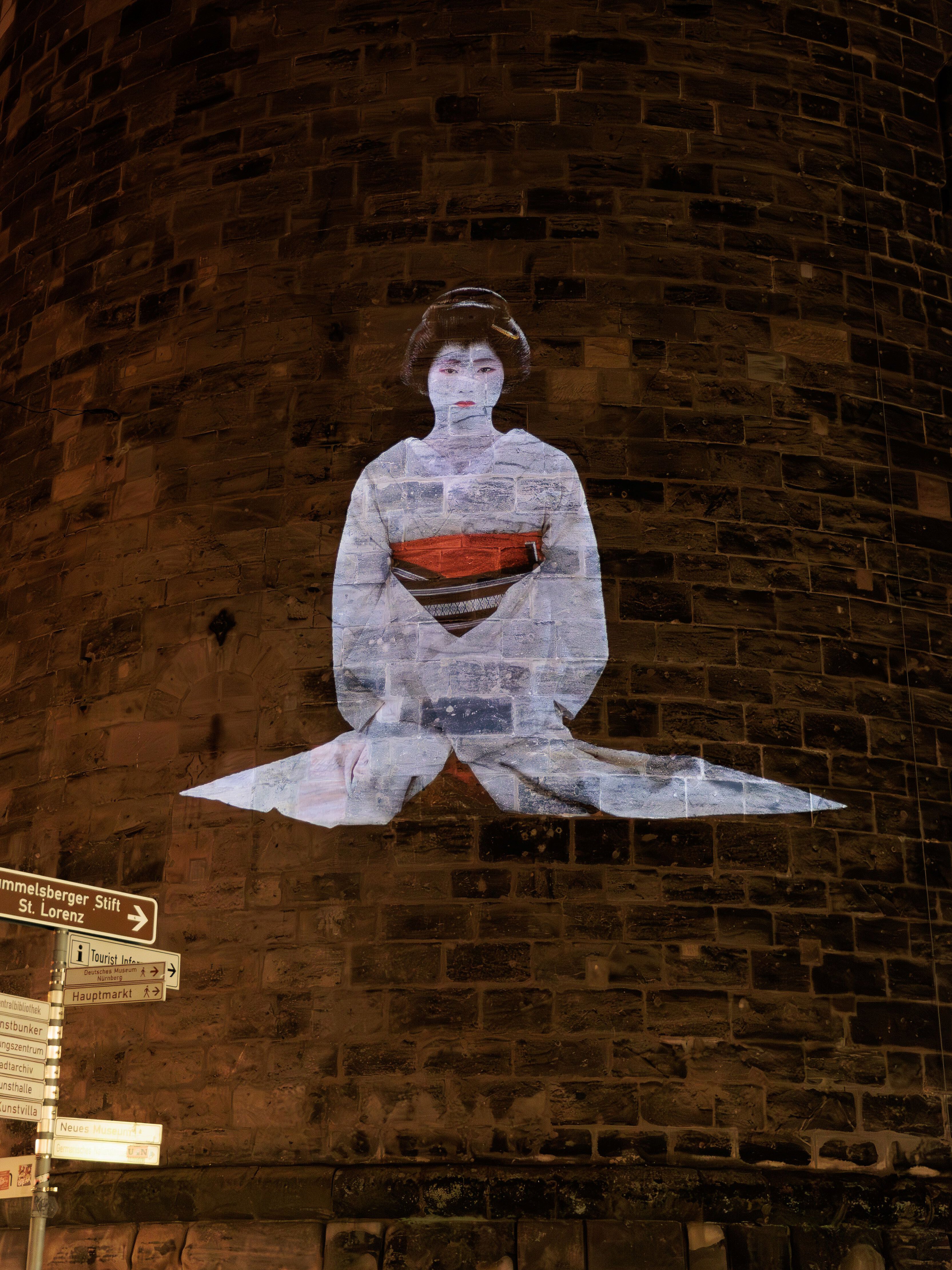 HD-Projektion einer sitzenden Geisha mit traditionellem Kimono auf den runden Backsteinturm Frauentorturm in Nürnberg