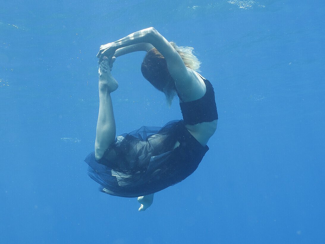 Frau untergetaucht im Wasser, formt einen Kreis mit ihrem Körper