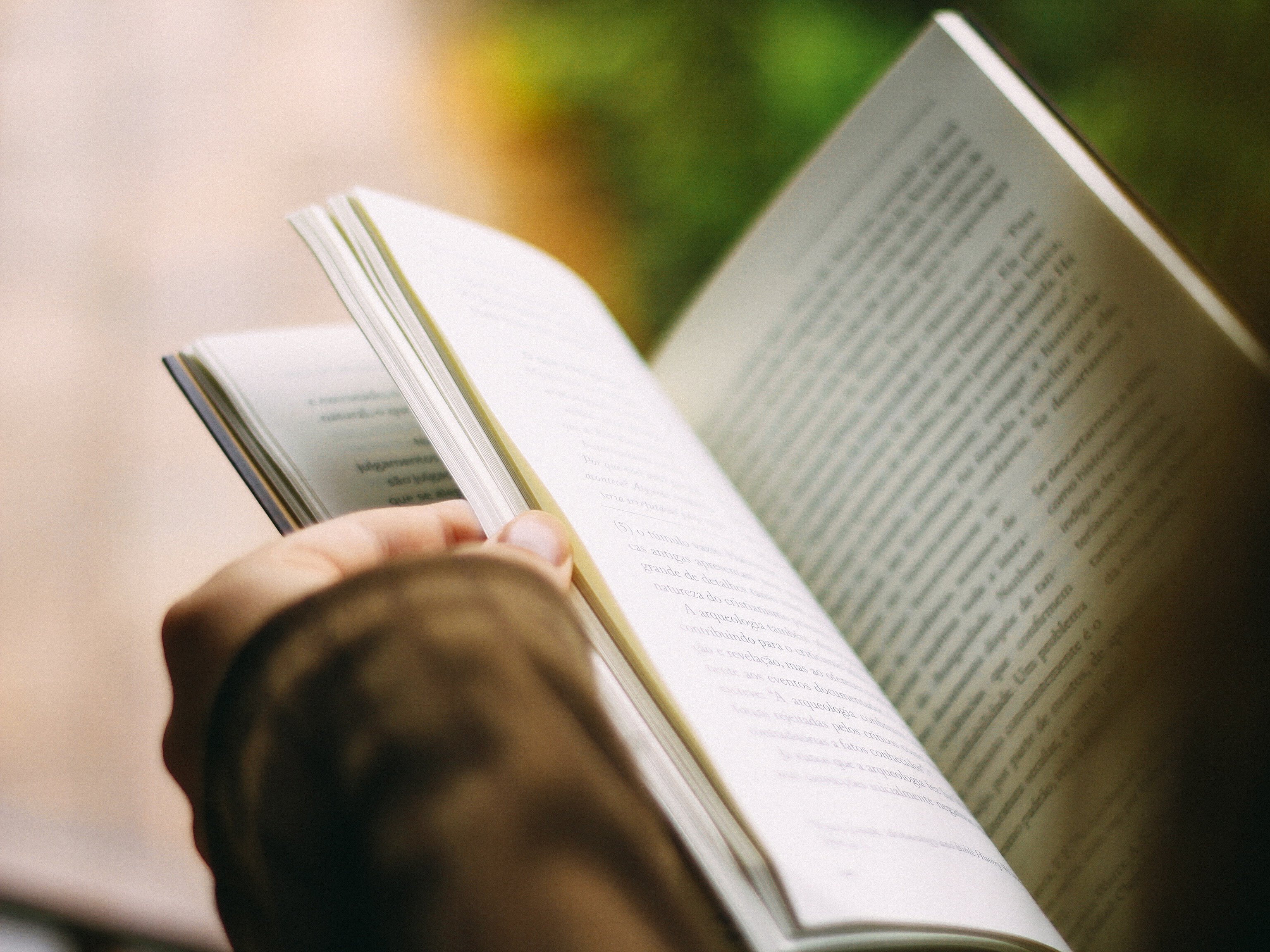 Person hält ein aufgeschlagenes Buch in der Hand.