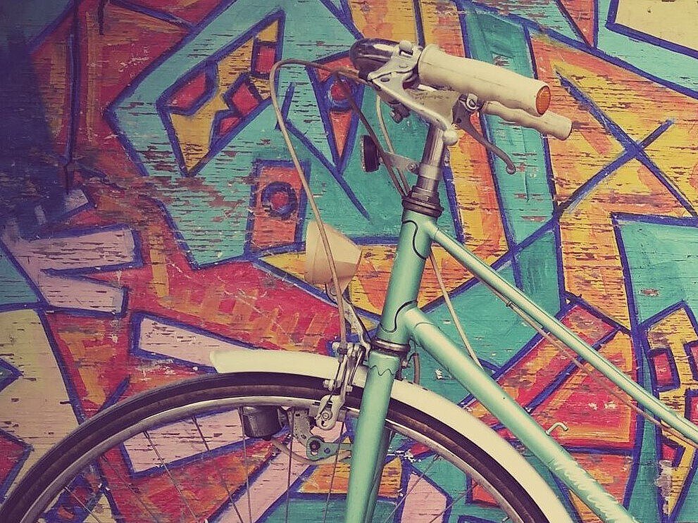 türkises Retro-Fahrrad vor einer bunt bemalten Holzwand