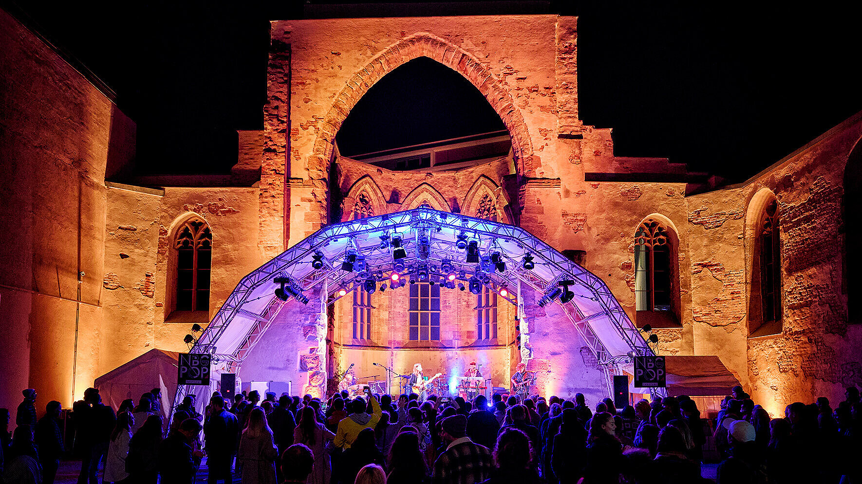 Bühne mit Beleuchtung vor einer beleuchteten gotischen Ruine und Publikum bei Nacht